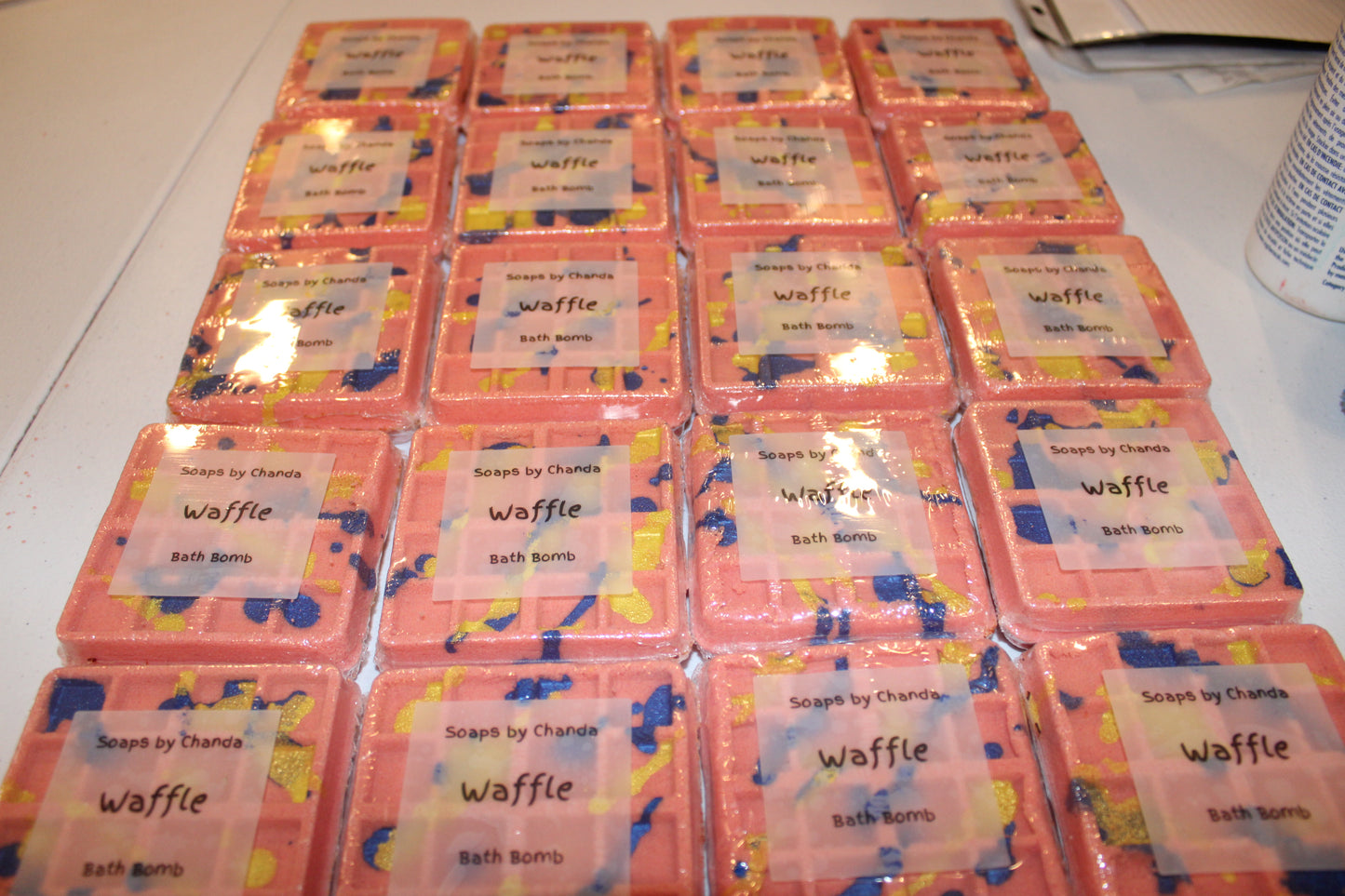 This is a picture of the waffle bath bombs lined up in the packaging. They are shrink wrapped with a clear label on the front . It says, "Soaps by Chanda". Underneath it says, "Waffle". And under that it says, "bath bomb".