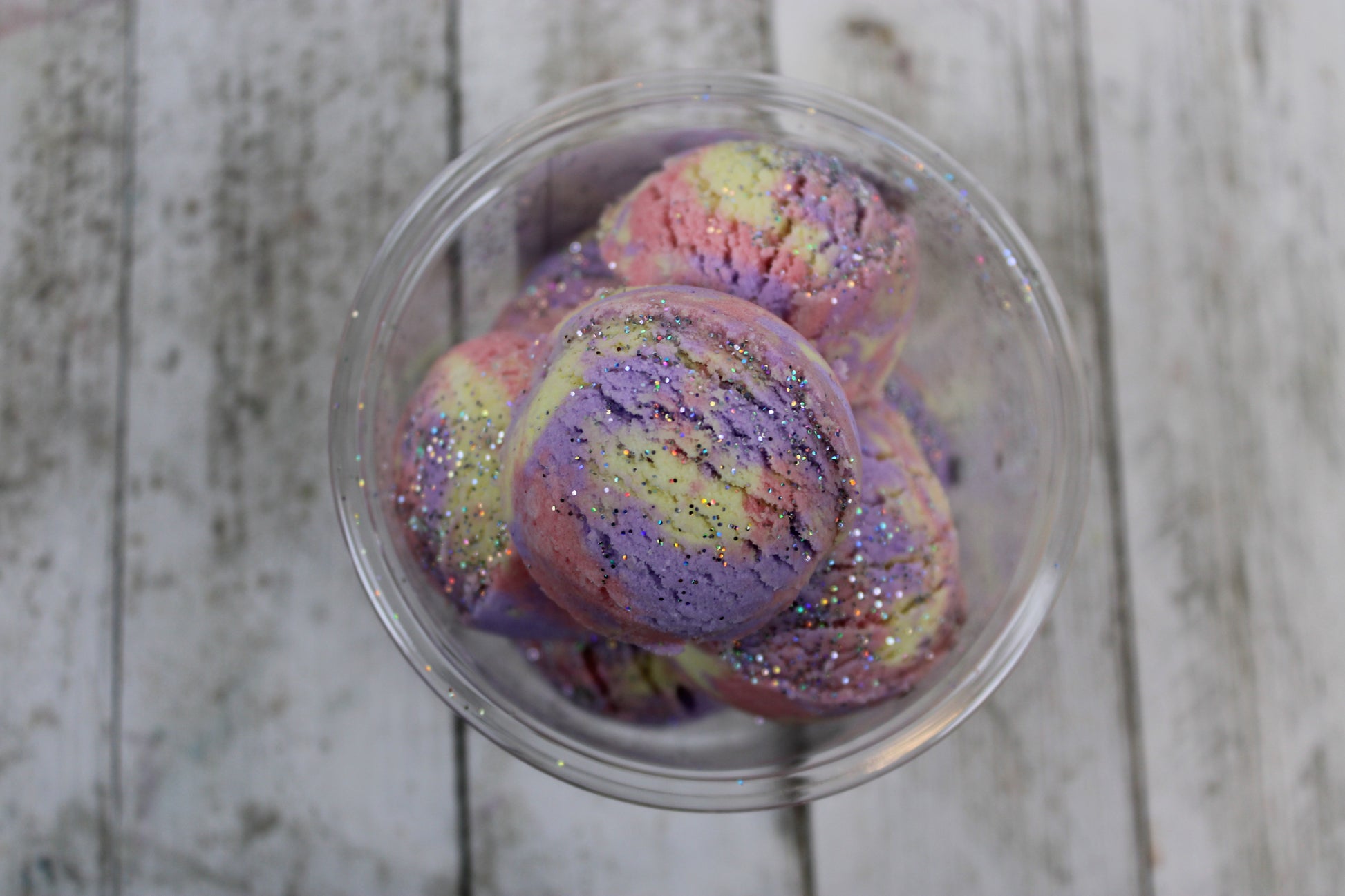 Top view of the purple, pink, and yellow bubble bars in their clear plastic container with dome lid.