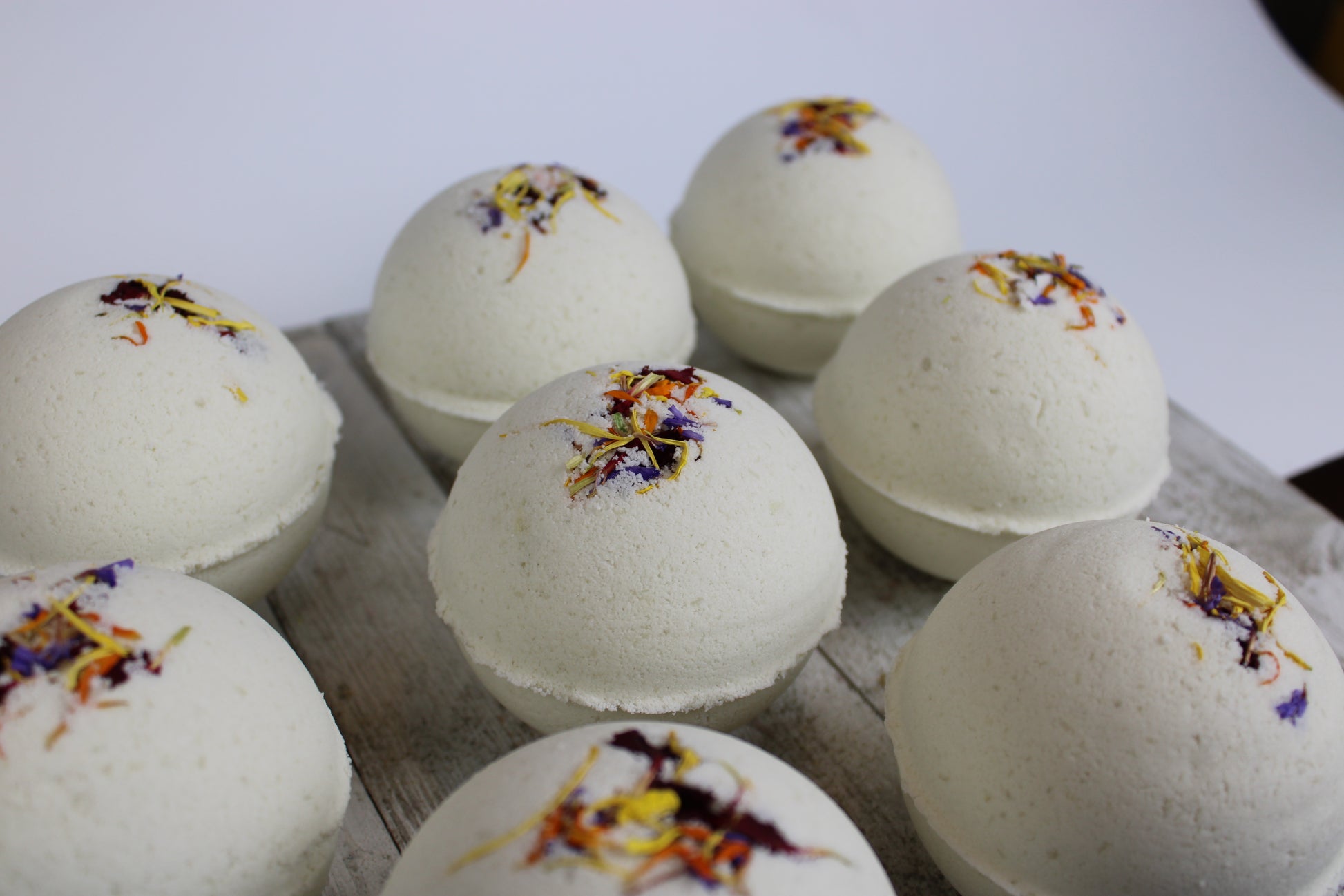 This is a bunch of the Cocoa Butter bath bombs lined up. They are white and have multiple colored botanicals
